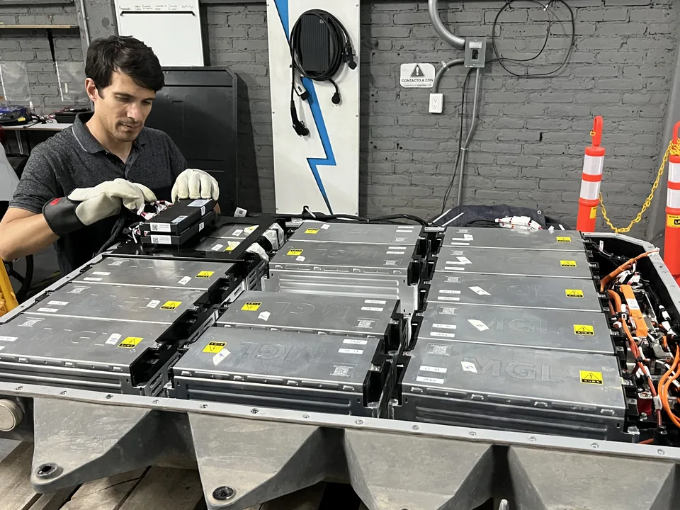 Técnico con guantes trabajando junto a los módulos de una batería de tracción abierta en el taller