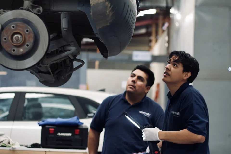 Dos técnicos de AlternEV inspeccionan el conjunto de freno de un vehículo elevado